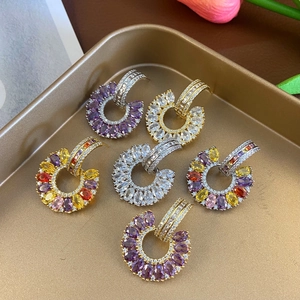 Close-up of C-shaped earrings set with colorful cubic zirconia in a gold jewelry tray