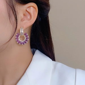 Detail of C-shaped gold earrings with purple marquise zircon stones on model