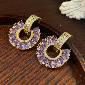 Detailed macro view of C-shaped gold earrings with purple marquise gems and pavé zircons