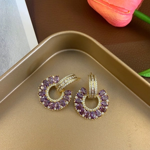 Detailed macro view of C-shaped gold earrings with purple marquise stones and zircon pavé
