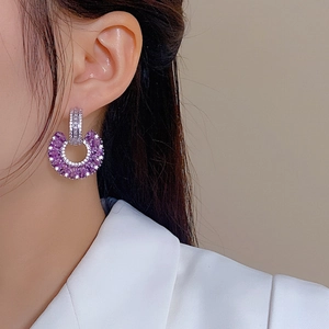 Close-up of elegant silver U-shaped earrings with purple teardrop zirconia on model