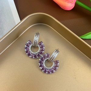 Macro detail of C-shaped earrings featuring purple marquise stones and gold plating