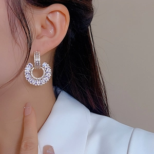 Close-up of elegant gold C-shaped earrings with marquise zircon stones worn by a model