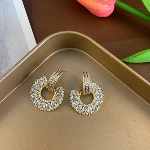 Detail of gold C-shaped earrings with micro-paved zircons on a golden display tray