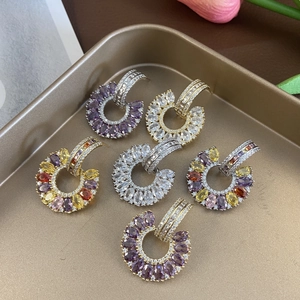 Macro shot of colorful zircon C-shaped drop earrings arranged on a gold metal jewelry tray