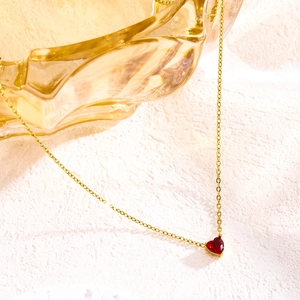 Golden heart necklace with red July birthstone crystal on a textured white surface