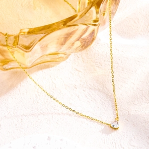 Close-up of golden chain necklace featuring a heart-shaped clear gemstone pendant