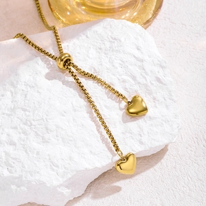 Detail of adjustable gold box chain with polished heart pendants on white stone