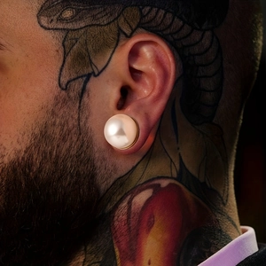 Macro detail of large cream pearl ear plug expansion on tattooed model's ear