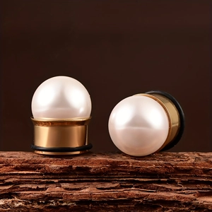 Macro view of stainless steel ear plugs with white pearls and golden bases on wood