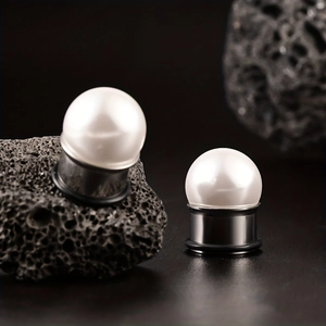 Detailed view of stainless steel ear plugs with white pearl tops on black volcanic rock