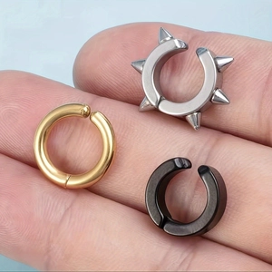 Detalle de orejeras de acero inoxidable en dorado, negro y plateado sobre una mano
