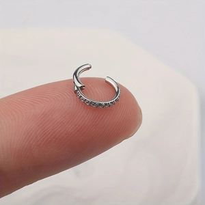 Macro shot of a 316L stainless steel hinged segment ring with cubic zirconia stones on fingertip