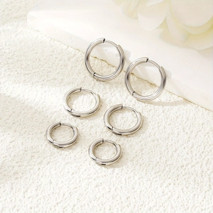 Three pairs of minimalist stainless steel hoop earrings in different sizes on white texture