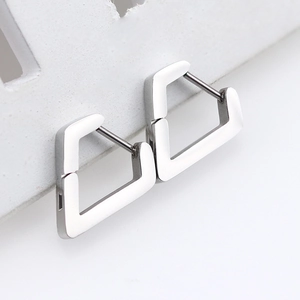 Macro shot of silver geometric stainless steel huggie earrings on a white textured stand
