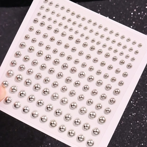 Detail of assorted silver faux piercing studs on white card over black glitter background