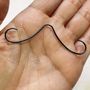 Close-up of a creative black mustache-shaped nose ring held in a palm for size reference
