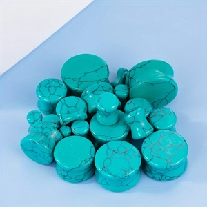 Polished turquoise stone ear plugs set with natural black marble texture on blue surface