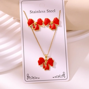 Close-up of red enamel bow necklace and stud earrings set on a stainless steel card