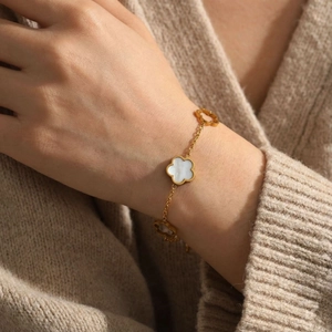 Détail macro du bracelet trèfle doré avec nacre blanche sur fond en maille beige