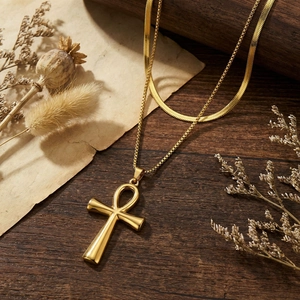 Golden double-layer Ankh cross necklace with box and snake chain design on vintage wood