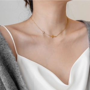 Detail einer minimalistischen Goldkette mit Kreuz und Zirkonia-Anhänger am Hals des Models