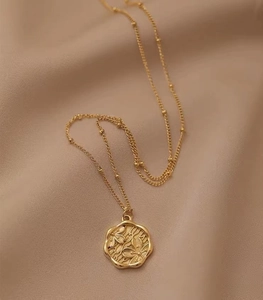 Detailed view of an 18K gold plated circular flower pendant on a beaded necklace chain