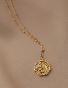 Close-up of 18K gold plated necklace with embossed floral pendant on silk fabric