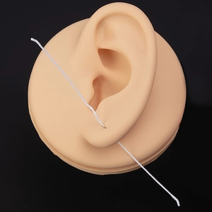 Detail showing white ear piercing cleaning floss passing through a silicone ear model