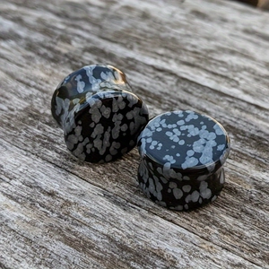 Macro shot of polished snowflake obsidian ear plugs on a rustic grey wooden background