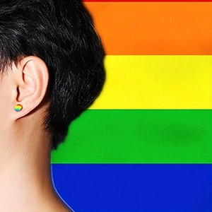 Detail view of round rainbow stainless steel studs worn on ear with vibrant color pattern