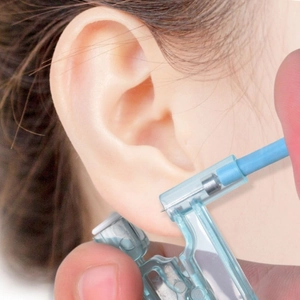 Close-up of disposable ear piercing gun with steel stud being applied to earlobe