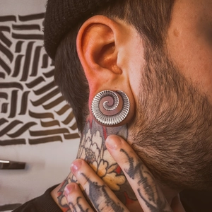 Makroaufnahme einer silbernen Spiral-Ohr-Expander mit radialen Streifen am Modellohr