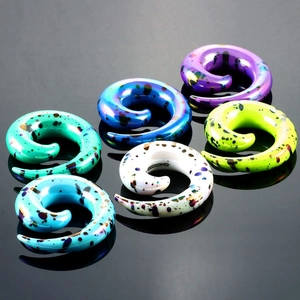 Colorful acrylic spiral ear tapers with black speckled patterns on a reflective surface