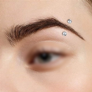 Dettaglio ravvicinato di un piercing al sopracciglio minimalista in acciaio con sfere