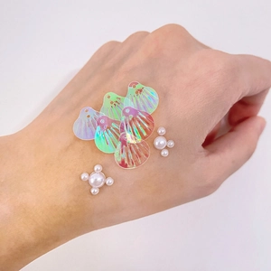 Lot de paillettes coquillages irisés et perles blanches, présenté sur main pour l'échelle