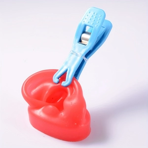 Blue plastic body piercing forceps clamping a red silicone ear model on white background