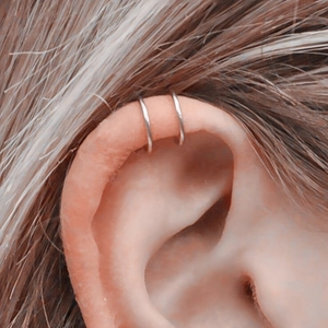 Close-up of minimalist silver stainless steel lip rings worn as ear cartilage cuffs