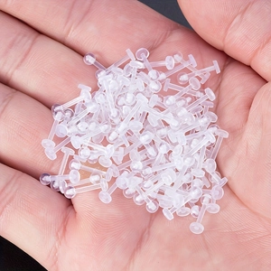 Close-up of bulk transparent acrylic labret retainers held in a hand for body piercing