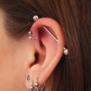 Detalle de un piercing industrial de acero inoxidable y aros de cartílago en la oreja