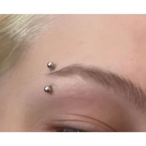 Close-up of curved stainless steel eyebrow piercing ring with ball ends worn on a model