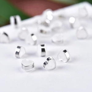 Detail of silver heart-shaped DIY earring backs with white enamel finish on a white background