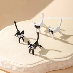 Detalle de pendientes de gato en blanco y negro con diseño 3D sobre placa de piedra