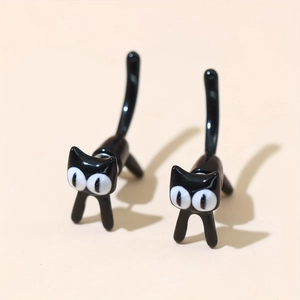 Detalle de pendientes de gato negro en 3D con acabado brillante sobre fondo beige