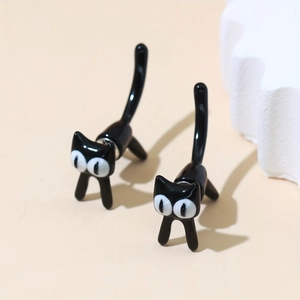 Detalle de pendientes de gato negro en 3D con ojos grandes sobre fondo minimalista
