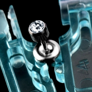 Macro shot of stainless steel piercing stud with round zircon in disposable holder