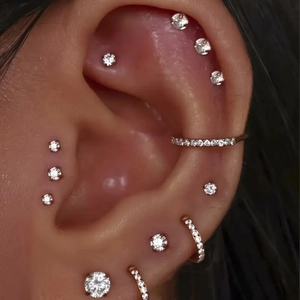 Macro view of crystal stud earrings and silver hoop clickers on various ear piercing points