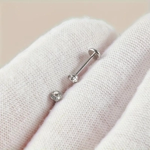 Macro shot of silver labret stud with clear rhinestone crystal held in gloved hands