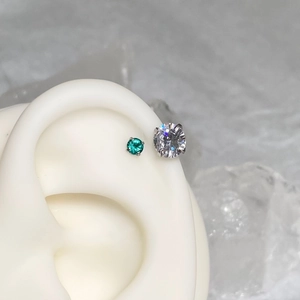 Macro shot of a 4-prong set green emerald and clear zircon stud earring on ear