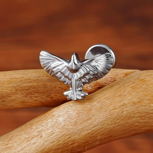 G23 titanium eagle labret stud with detailed wing texture on a natural wood branch